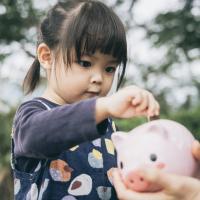 Little girl putting coins in a piggy bank.