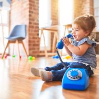 Beautiful toddler sitting on the floor playing with vintage phone at kindergarten.