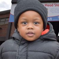 Smiling little boy bundled up in from of Early Head Start center 