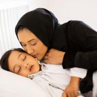 caring muslim mother kissing baby boy while he is asleep 
