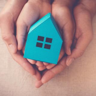 Parent and child hands holding a small cardboard blue house.