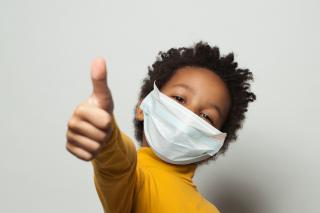 Thumbs up from a masked young child. 