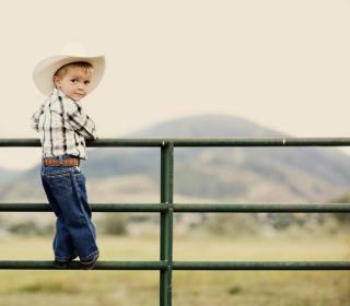 Young child on a fence with cowboy hat.