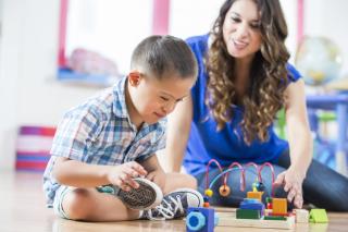 Little boy with Downs Syndrome and child care provider playing together. 