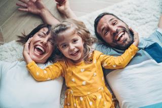 Happy parents and toddler laying on floor.