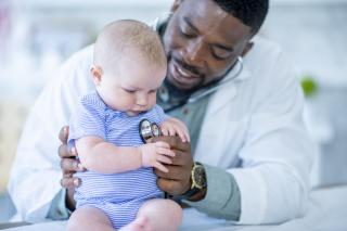 African American male doctor listening to a white baby's heart. 