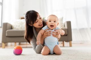 A woman with dark hair holds a smiling baby in a living room