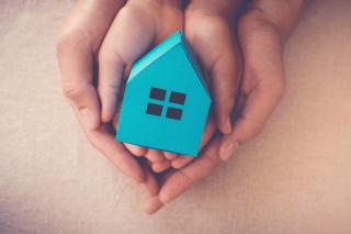 Parent and child hands holding a small cardboard blue house.