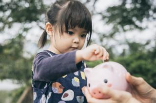 Little girl putting coins in a piggy bank.