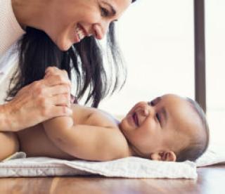 Happy mother playing with baby while changing his diaper. Smiling young woman with baby son on changing table at home. Close up of cheerful mom and toddler boy playing together. 