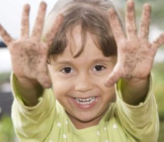 Beautiful little girl having fun outdoors and showing her dirty hands 