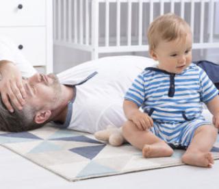 cropped shot of a tired father lying on the floor next to his little baby 