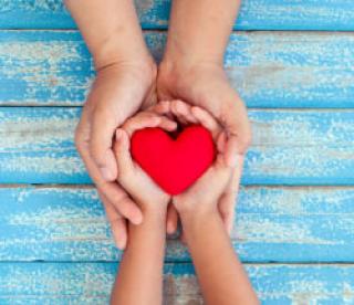 Red heart in child kid and mother hands on old blue wooden table in vintage retro style 