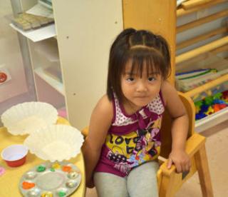 Young girl in classroom sits at table with empty objects 