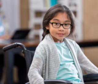 Pretty elementary age girl in wheelchair waits in doctor's office waiting room. 