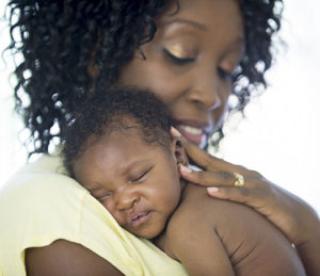 A mother is holding her newborn baby in her arms. They child is sleeping against her shoulder. 