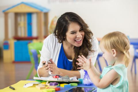 Update your record Cheerful female Hispanic teacher praises adorable blonde Caucasian little girl on accomplishing a project. The preschooler claps along with the teacher.